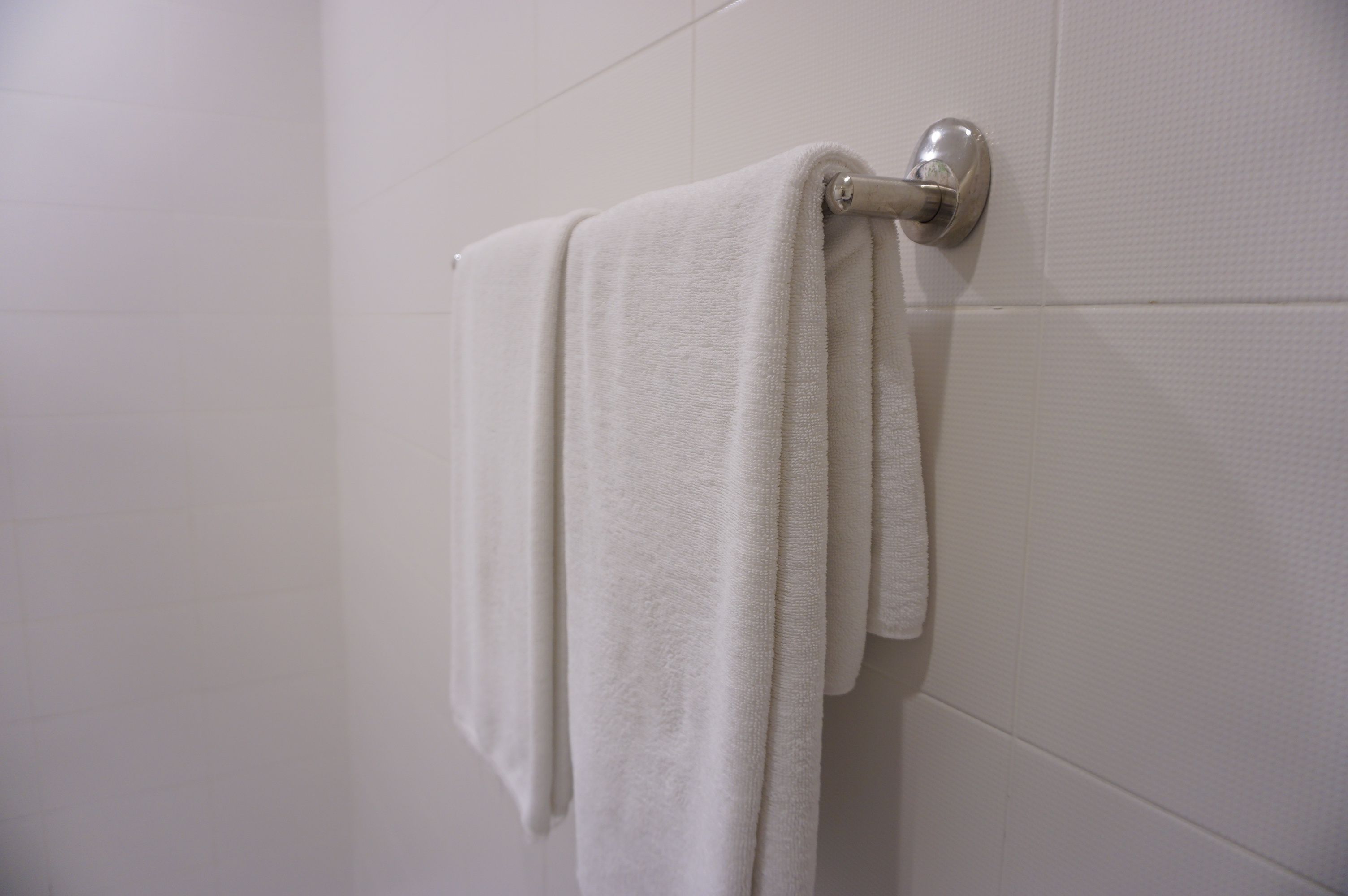 A white towel hanging on a metal towel rack against a white tiled wall.
