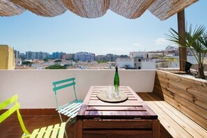 En balkon med et træbord og stole, en flaske samt udsigt over bybilledet.