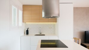 Une cuisine moderne avec des meubles blancs, une plaque de cuisson à induction noire, une hotte en acier inoxydable et un dosseret carrelé.