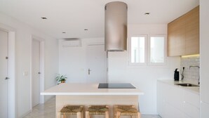 Une cuisine moderne dotée d’un îlot central, de tabourets en bois, d’une hotte en acier inoxydable et d’une fenêtre située au-dessus de l’évier.