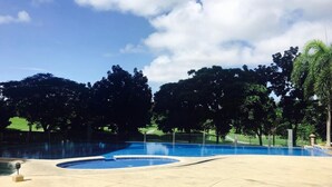 A swimming pool with a curved edge, surrounded by trees and a clear sky. - 2 Bedroom Bellagio Towers by Stays PH (Taguig)