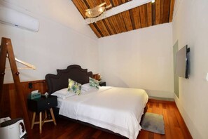 A bedroom with a wooden ceiling, a bed with white bedding, a nightstand, a lamp, and a TV mounted on the wall.
