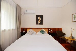 A hotel room with a large bed, a wooden headboard, a small table with a vase, and a chair.