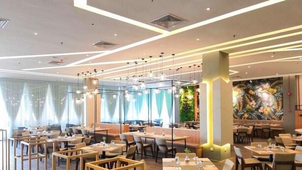 Ein modernes Restaurant mit mehreren Essbereichen, Holzmöbeln und dekorativer Beleuchtung.
