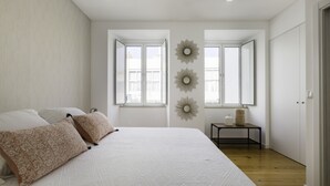 A bedroom with a large bed, two windows, a small table, and a wardrobe. - Tile House 95, Penha de França (Lisboa)
