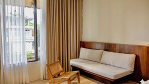 A room with a sofa, a chair, a window with curtains, and a view of greenery outside. - Soleil House (Hue)