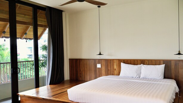 A bedroom with a wooden bed, a ceiling fan, and a view of greenery outside. - Soleil House (Hue)