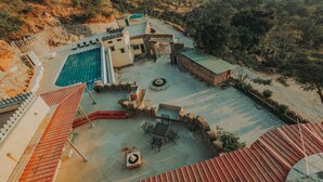 Vista aérea de un resort con piscina, mobiliario exterior y montañas al fondo.