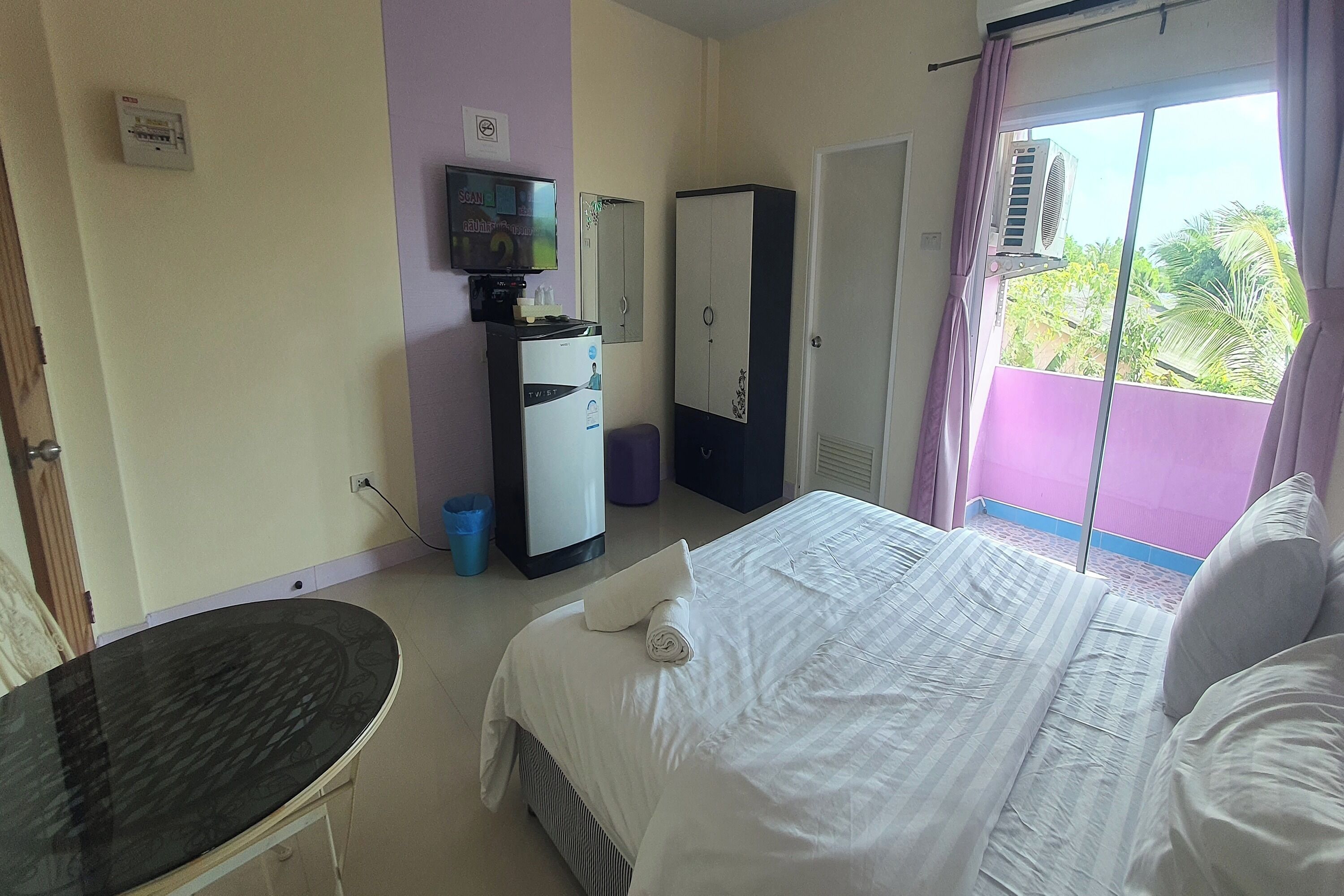 A hotel room with a bed, a desk, a wardrobe, a television, and a window with a view of greenery.