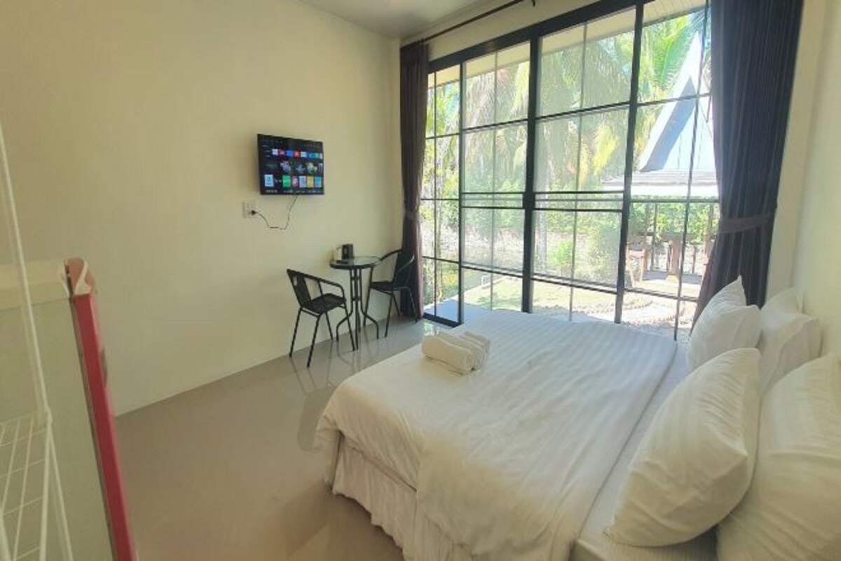 A hotel room with a large bed, a TV mounted on the wall, a small table with chairs, and a window with curtains.