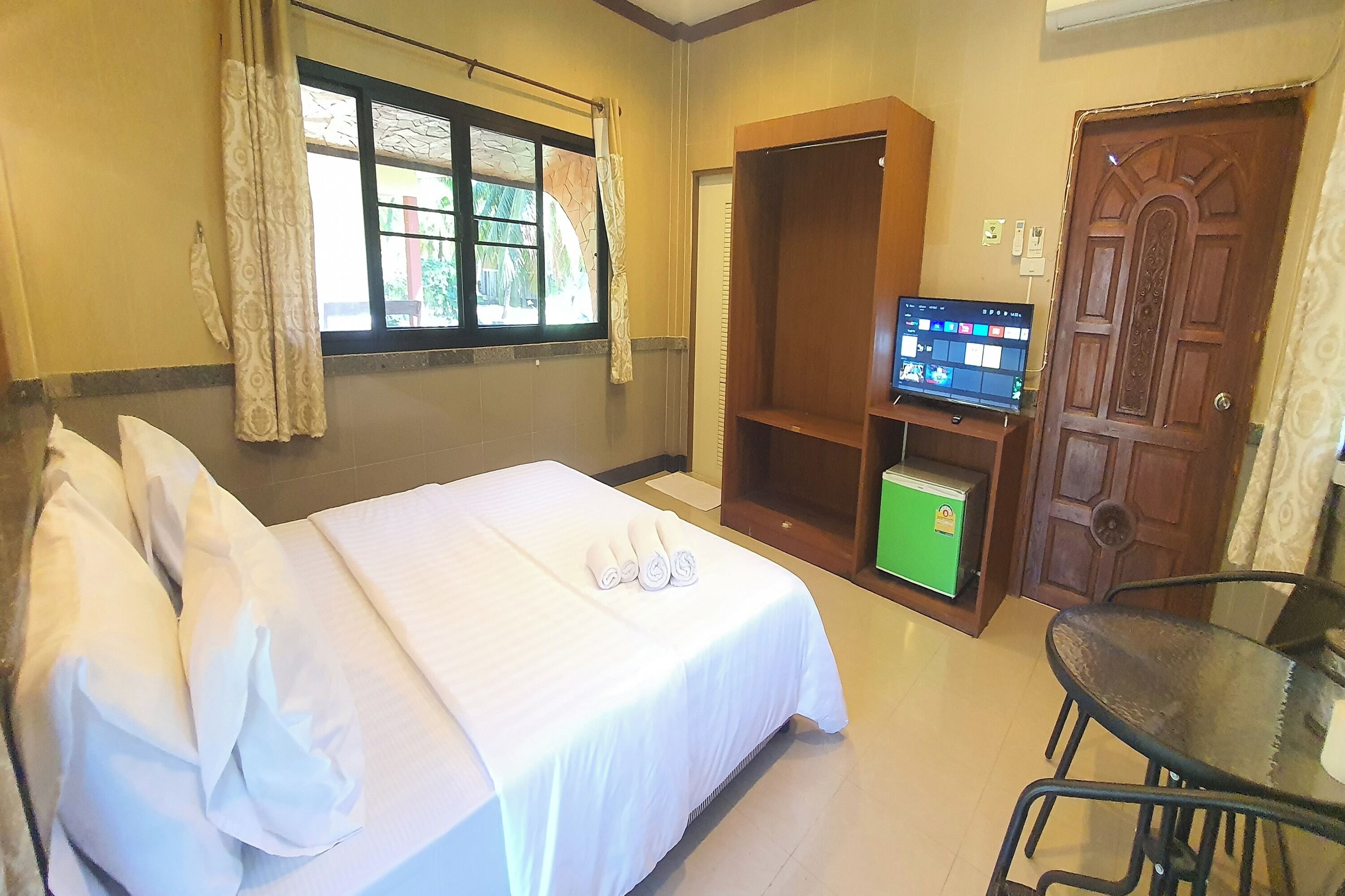 A hotel room with a bed, a television, a green minibar, and a wooden door.