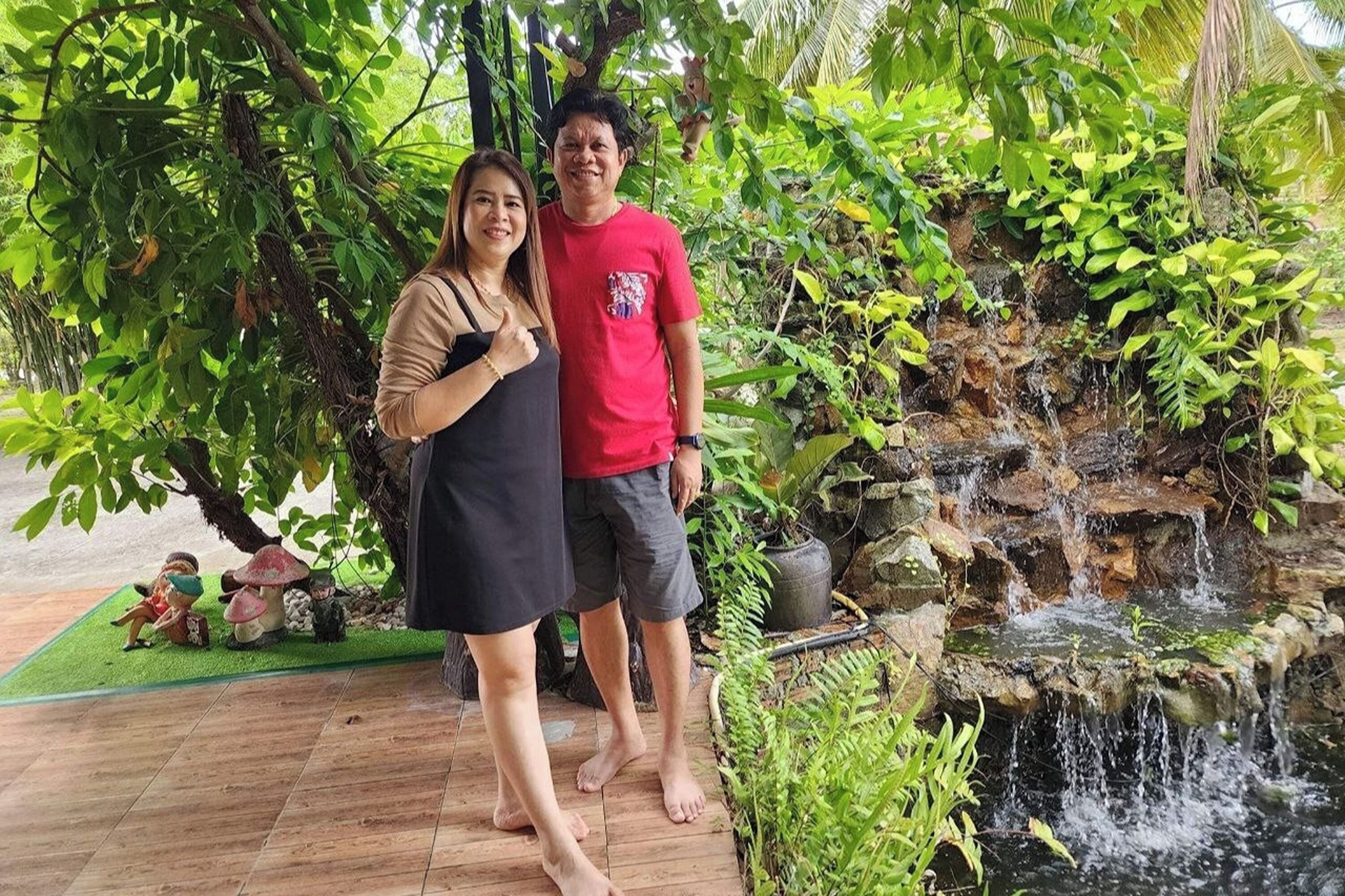 Un hombre y una mujer están de pie en un jardín con una pequeña cascada y abundante vegetación.