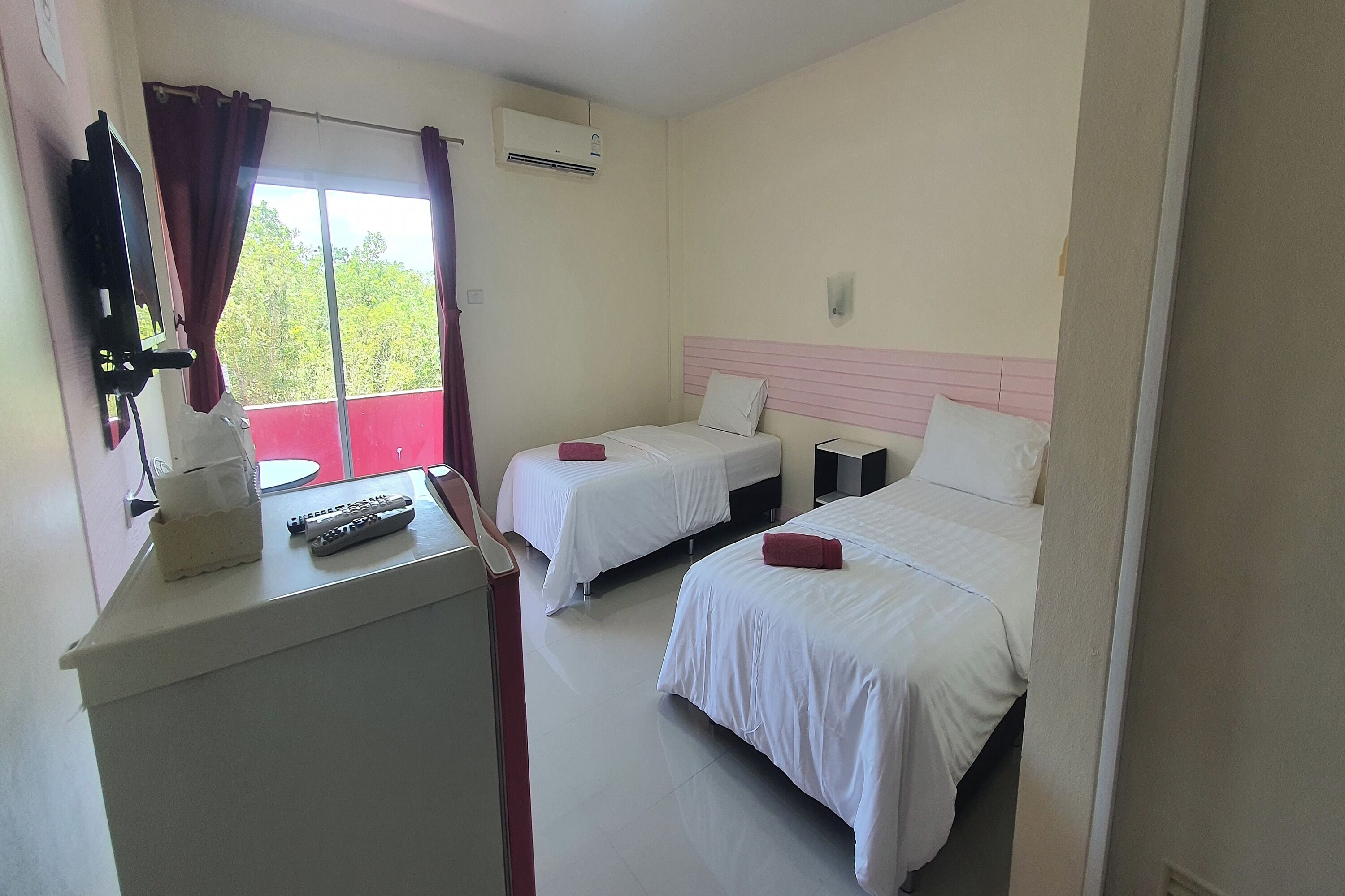 A hotel room with two beds, a desk with a remote control, and a window with curtains.