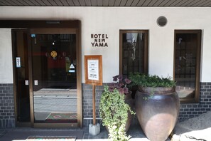 La entrada del Hotel New Yama, con una planta grande en maceta y un felpudo de bienvenida.