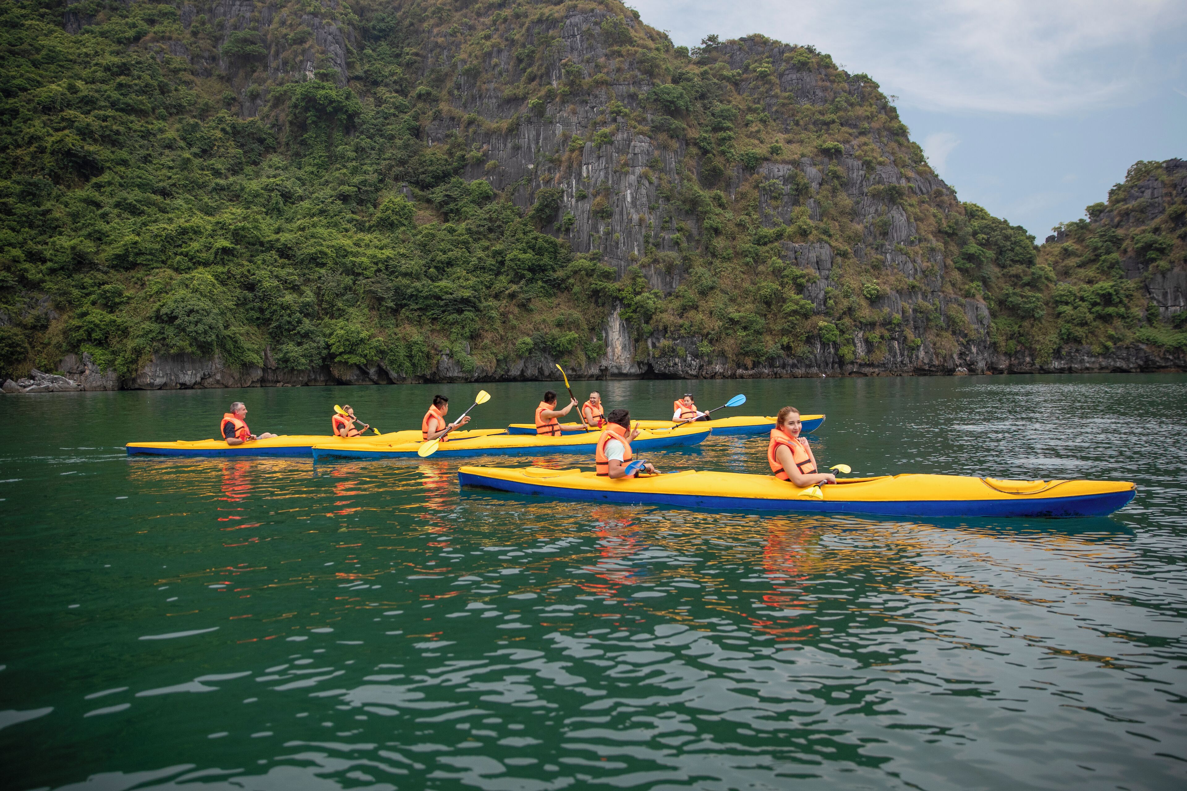 A group of people in yellow kayaks on a calm body of water with a mountainous backdrop.