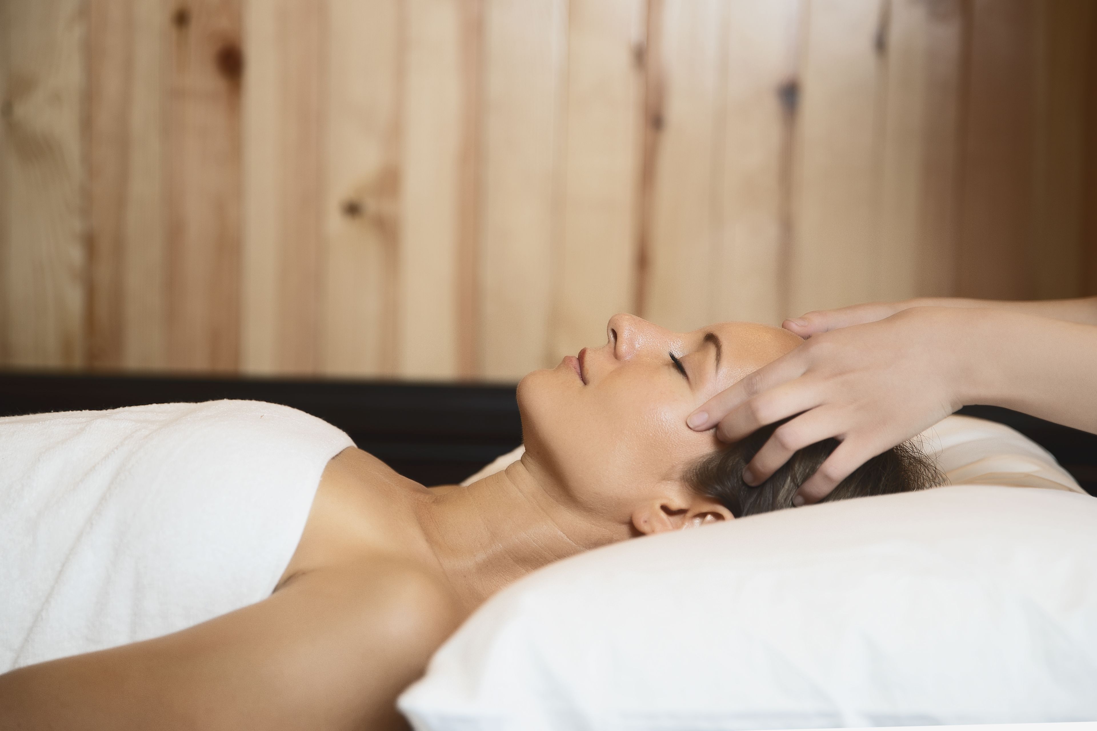 A person lying on a bed with a wooden headboard, receiving a massage.