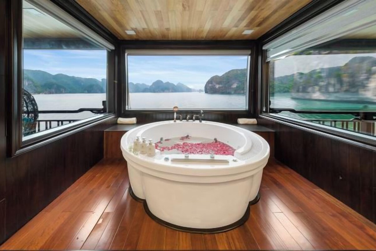 A large bathtub with a view of a river and mountains through large windows.