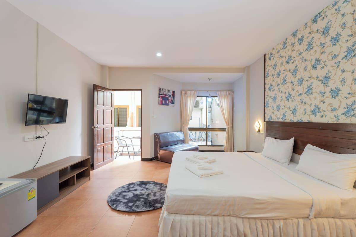 Une chambre d’hôtel avec un grand lit, un téléviseur fixé au mur, un bureau avec une chaise et une fenêtre avec des rideaux.