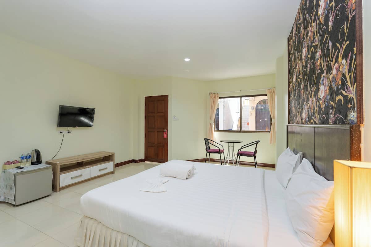 Une chambre d’hôtel avec un grand lit, un téléviseur fixé au mur, un petit bureau avec une chaise et une fenêtre avec des rideaux.