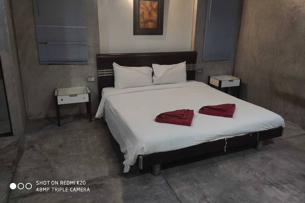 Une chambre d’hôtel comprenant un lit, deux tables de chevet, une petite table, une œuvre d’art accrochée au mur et une fenêtre avec des stores.