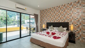 Quarto de hotel com uma cama grande, varanda e vista para palmeiras, e papel de parede estampado.