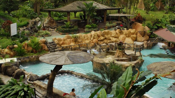 A tropical resort with a natural pool, wooden structures, and lush greenery. - Los lagos (La Fortuna)