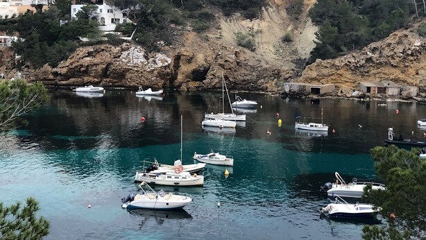 Un port de plaisance où sont amarrés plusieurs bateaux, entouré de falaises rocheuses et d’immeubles d’habitation.