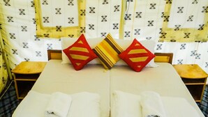 Cama doble con dos almohadas, una mesita pequeña y una silla en habitación con cortinas estampadas.