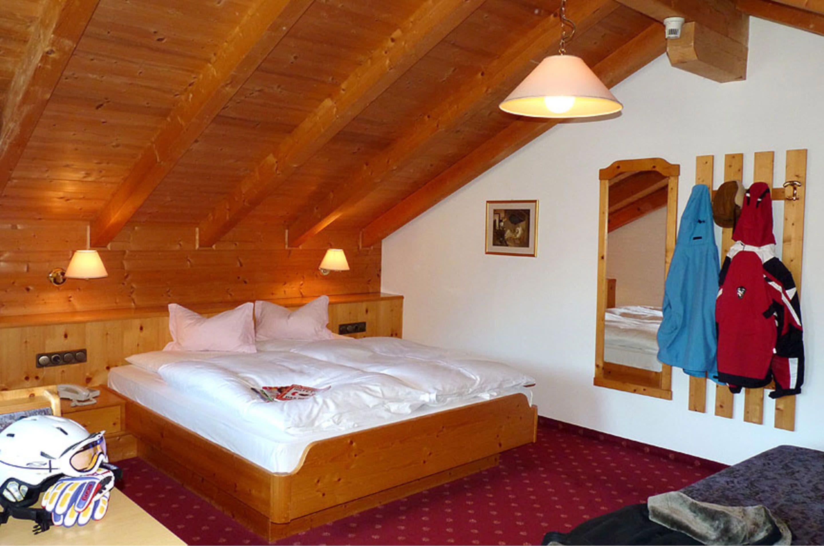 Ein Zimmer mit Holzrahmen, einem Einzelbett, einem Holz-Kopfteil und einem Spiegel, an dem Kleidung hängt.