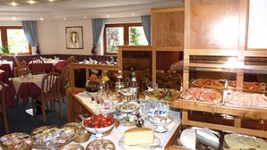 A buffet with various food items, including cheese, fruits, and meats. There are tables and chairs arranged for dining. - Hotel Fortuna (Ortisei)