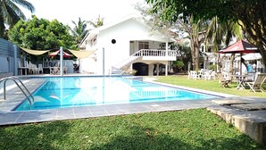 A swimming pool with a white building in the background, surrounded by greenery and outdoor seating. - Cinnamon Villa Negombo (Negombo)