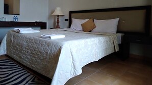 A neatly made bed with a quilted cover, a bedside lamp, and a brown pillow. - Cinnamon Villa Negombo (Negombo)