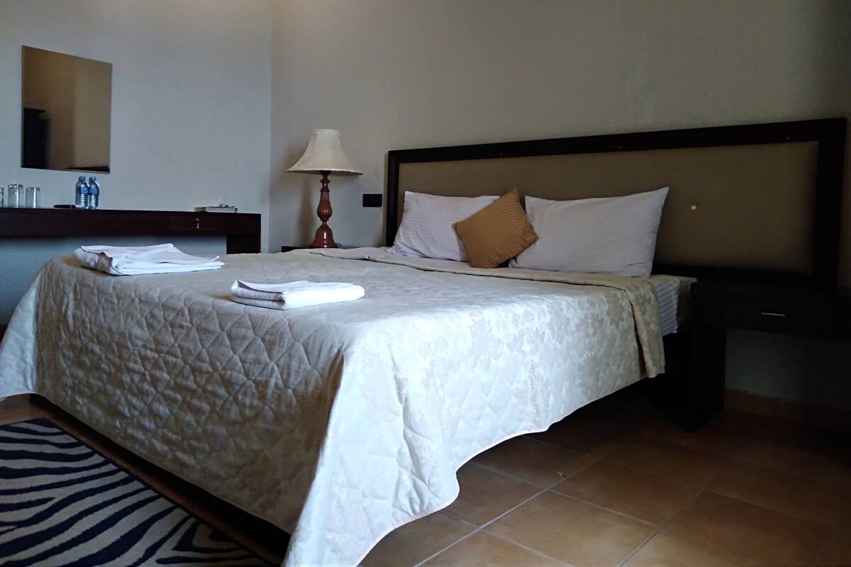 A neatly made bed with a quilted cover, a bedside lamp, and a brown pillow.
