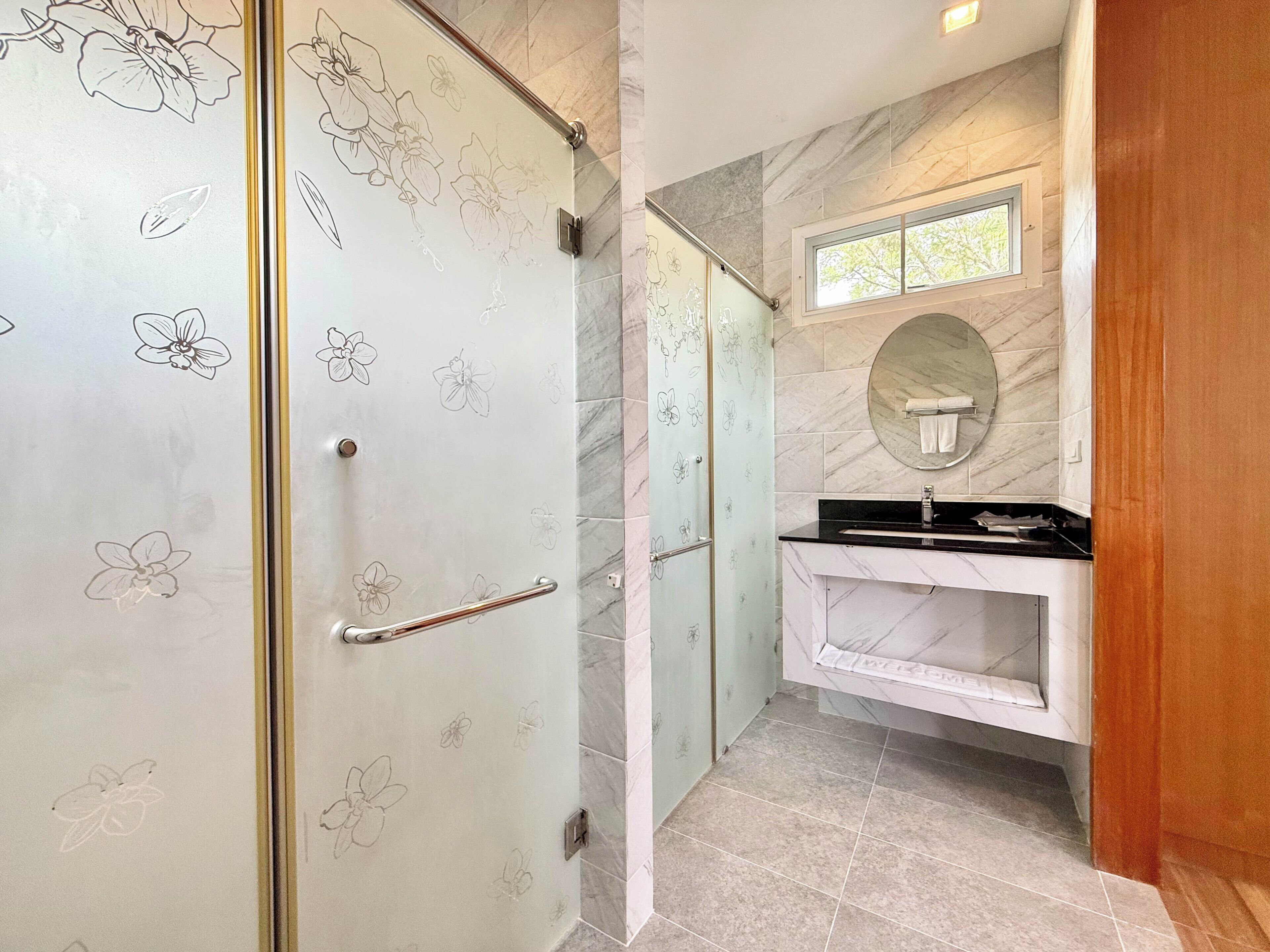 Une salle de bain avec une porte de douche en verre, un lavabo en marbre et un miroir.