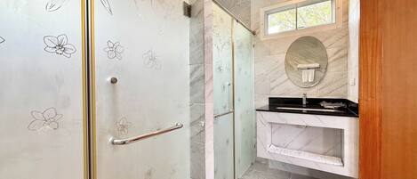 Une salle de bain avec une porte de douche en verre, un lavabo en marbre et un miroir.