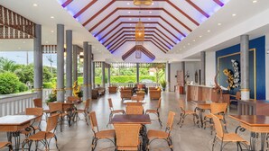 Un espacio interior amplio con varias mesas y sillas, un techo decorativo y vistas a la vegetación exterior.