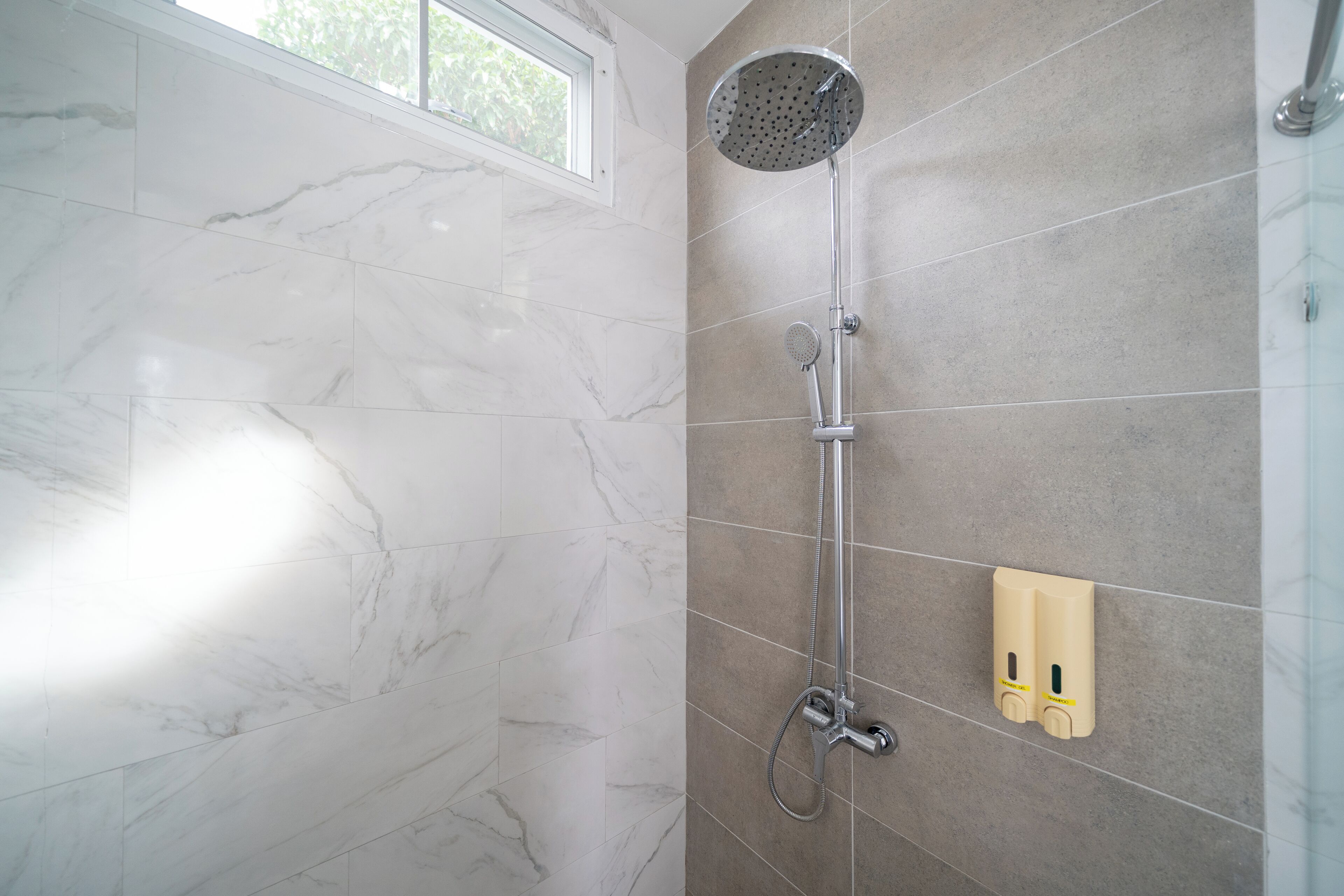 A shower with a handheld showerhead and a wall-mounted faucet, set against a backdrop of marble and beige tiles.