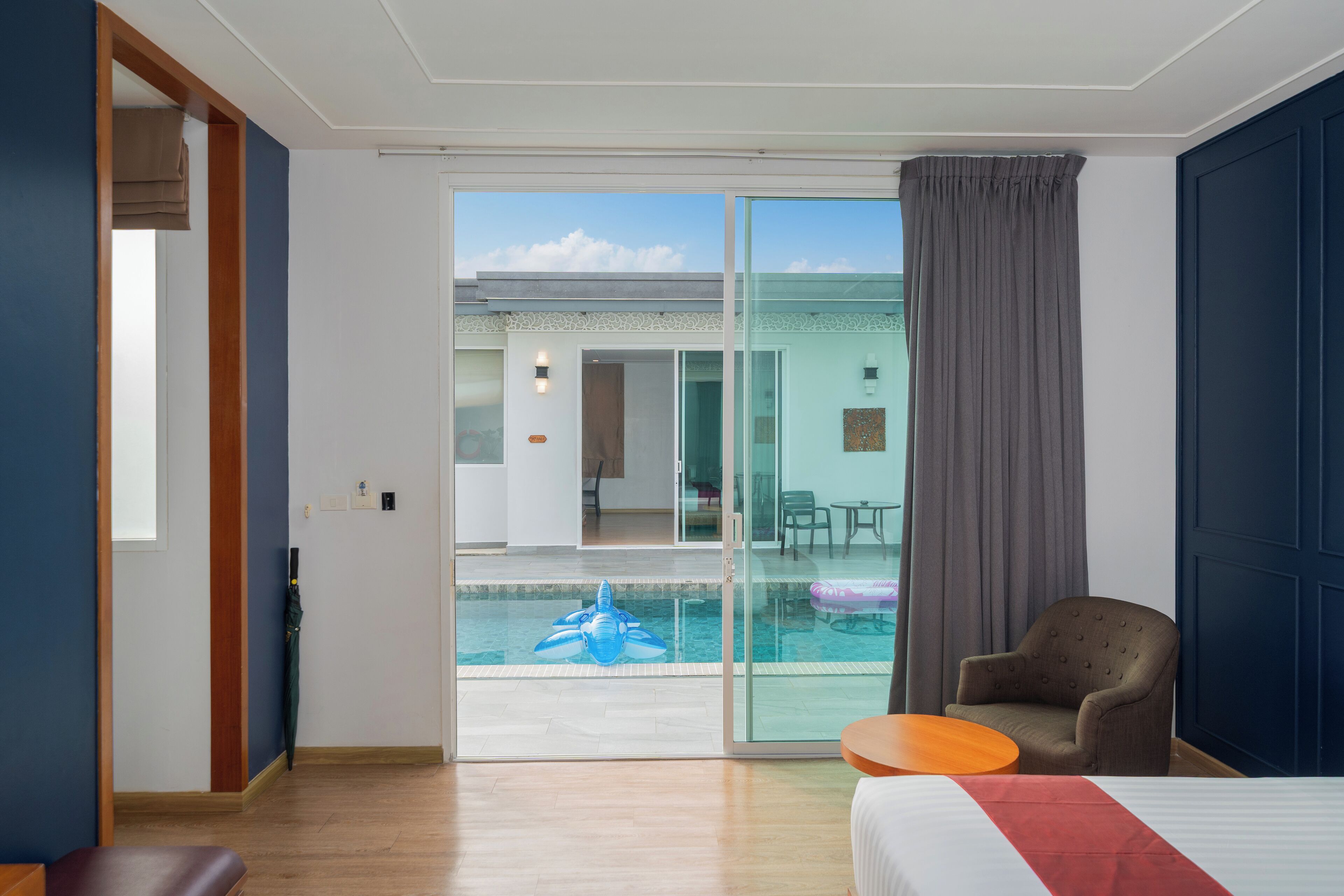 A hotel room with a bed, a small table, a chair, and a view of an outdoor swimming pool.