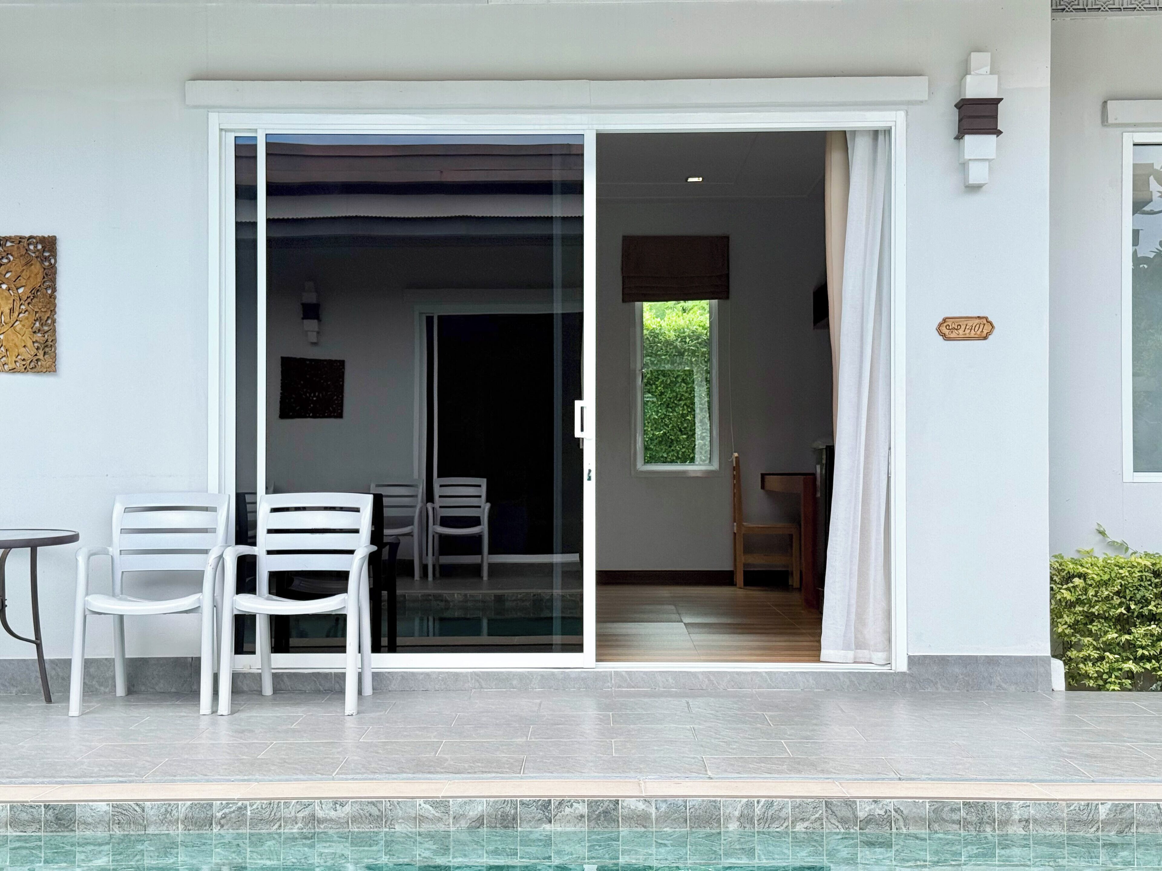 A modern outdoor seating area with a pool, a sliding glass door leading to an interior space, and a small window with a view of greenery.