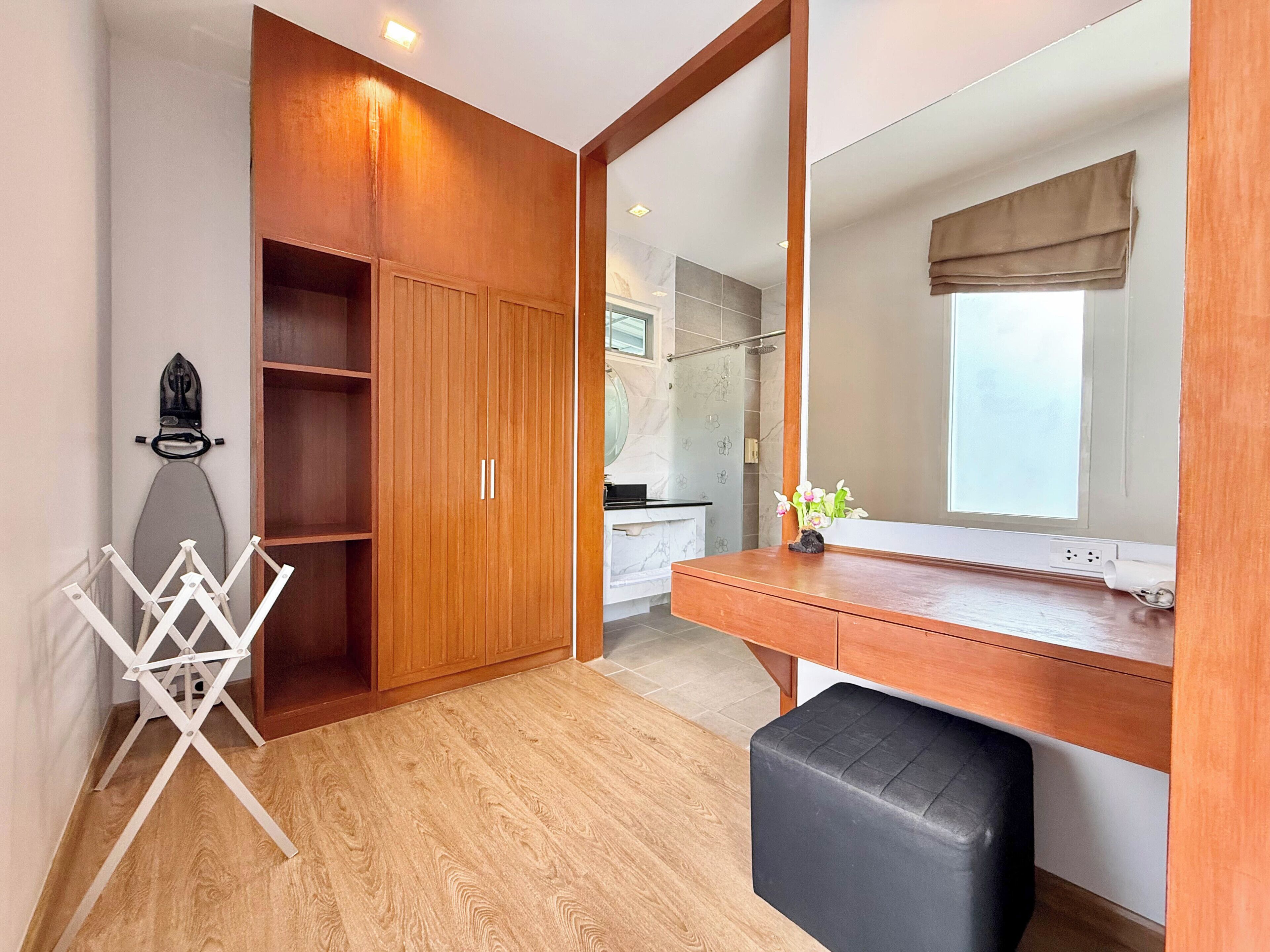 Una habitación con un armario de madera, un espejo, un escritorio con una silla negra y suelo de madera.