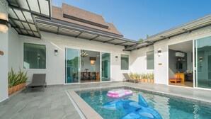 Una piscina con juguetes inflables, un patio cubierto y un comedor con mobiliario de exterior.