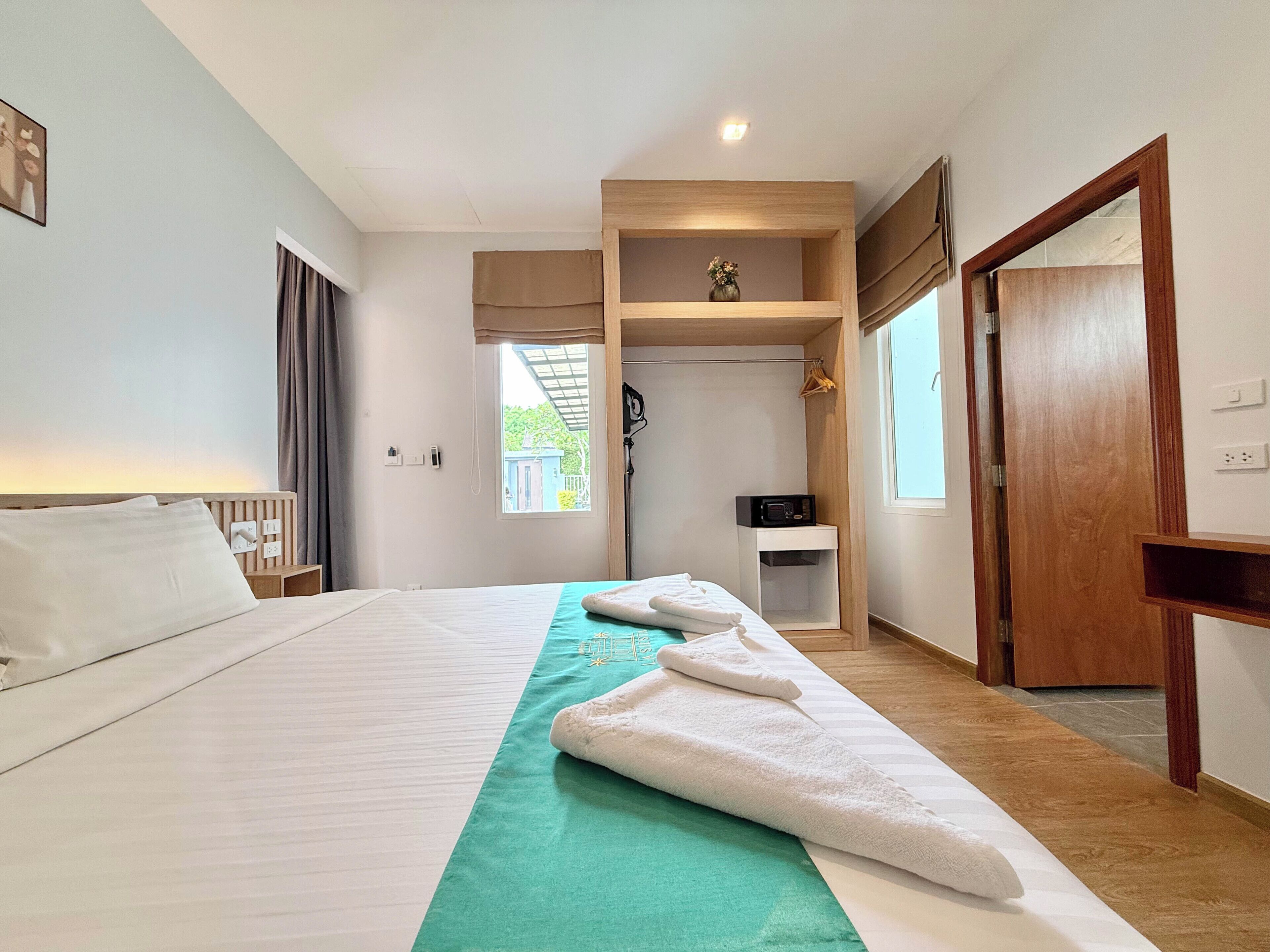 Een hotelkamer met een bed, een groene handdoekhouder, een klein tafeltje met een radio en een kledingkast.