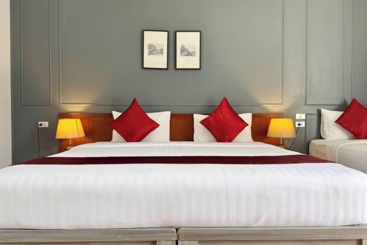 A hotel room with a large bed, two bedside lamps, and a headboard with red pillows.