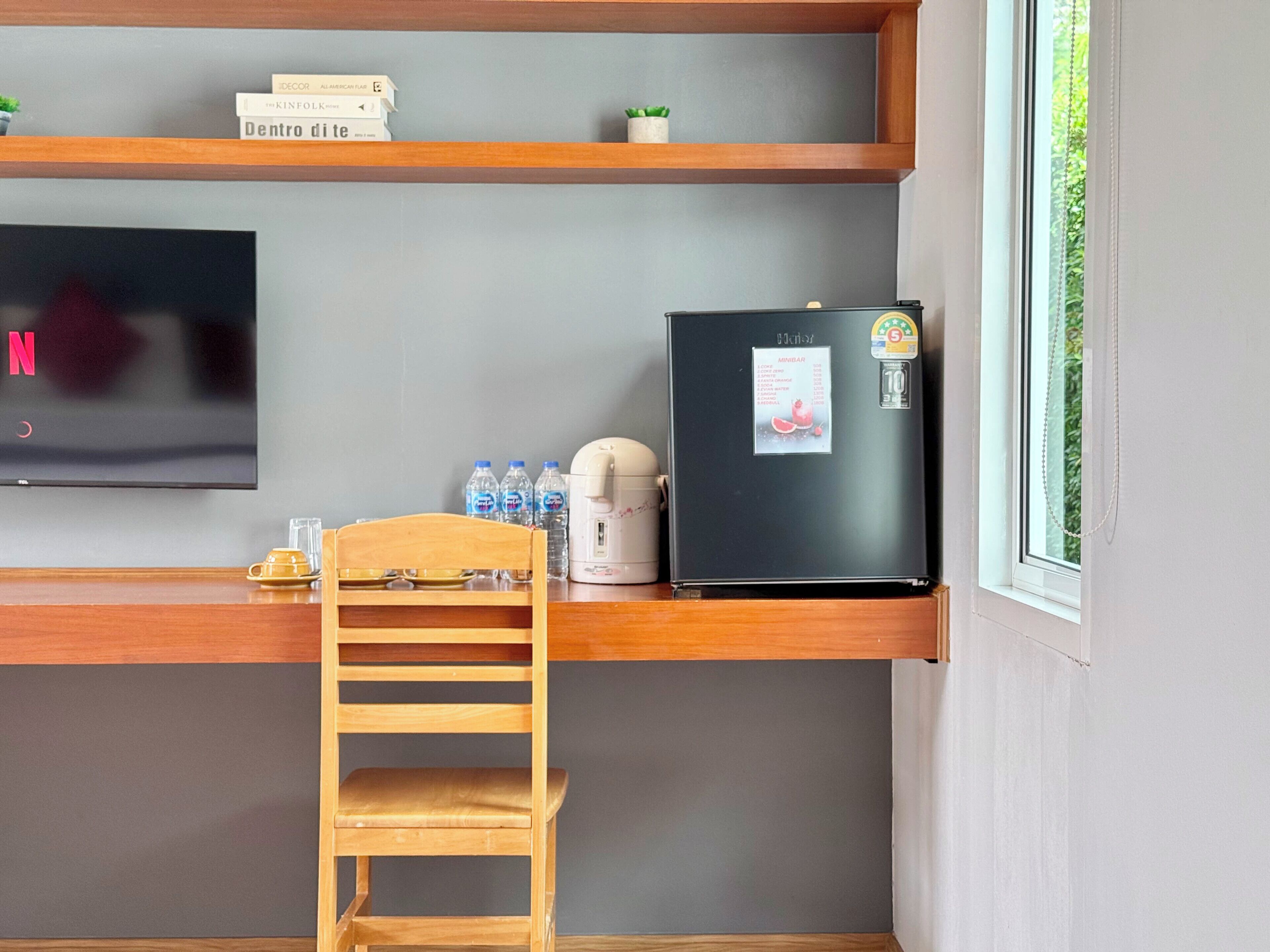 A kitchenette with a TV, refrigerator, water bottles, and a coffee maker.
