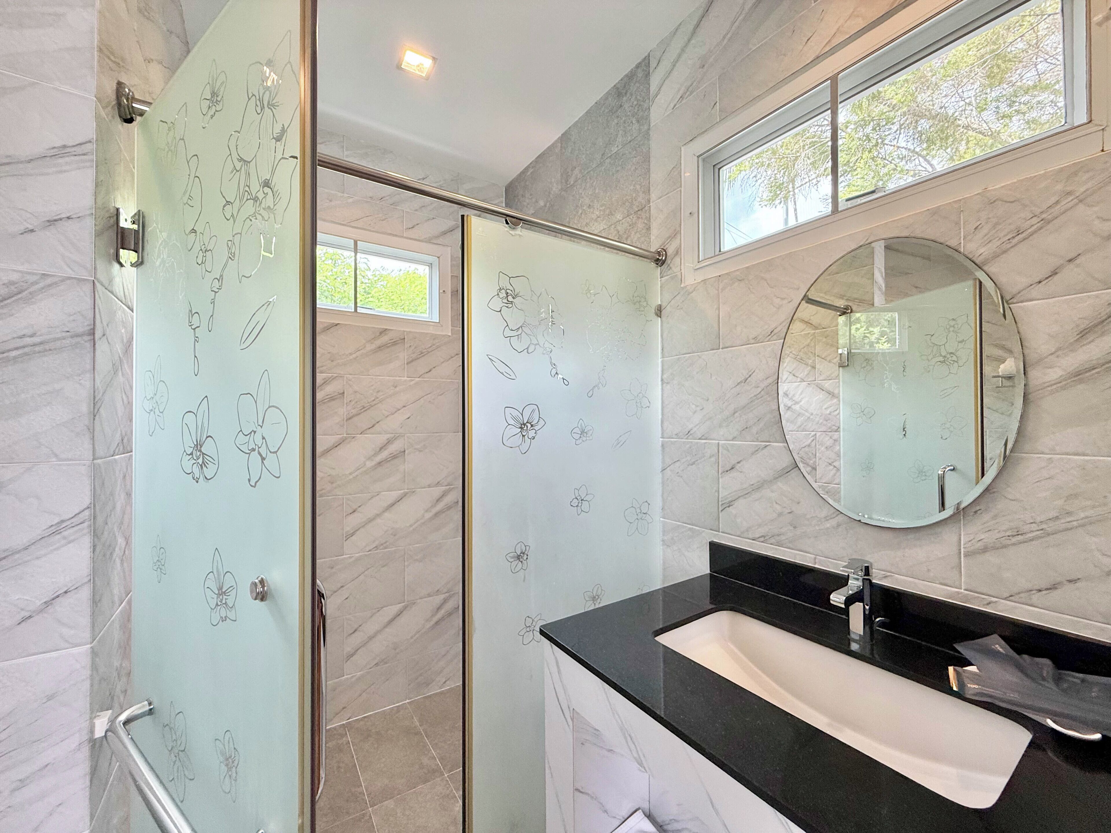 A modern bathroom with a glass shower door, a round mirror, and a black countertop sink.