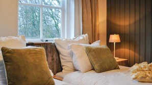Hotelkamer met een bed, kussens, een nachtkastje, een lamp en een raam met uitzicht op bomen.