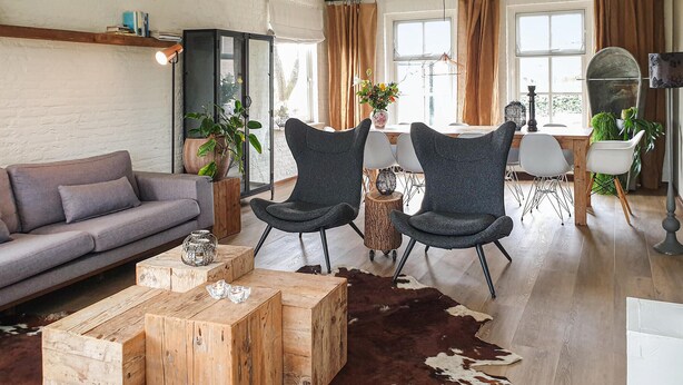 Een moderne woonkamer met een grijze bank, twee donkere fauteuils, een houten salontafel en een vachttapijt.
