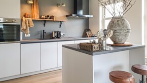 Een moderne keuken met een centraal eiland, houten barstoelen en een grote vaas op het eiland.