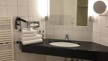 Un baño moderno con un lavamanos negro, azulejos blancos, un perchero con toallas dobladas, un secamanos y un espejo.