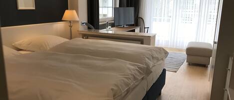 Habitación de hotel con una cama grande, un escritorio con computadora, una silla y una ventana con cortinas.